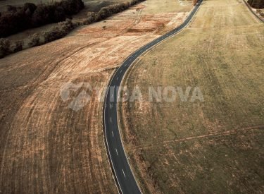 An aerial view of a long asphalt road surrounded by fields